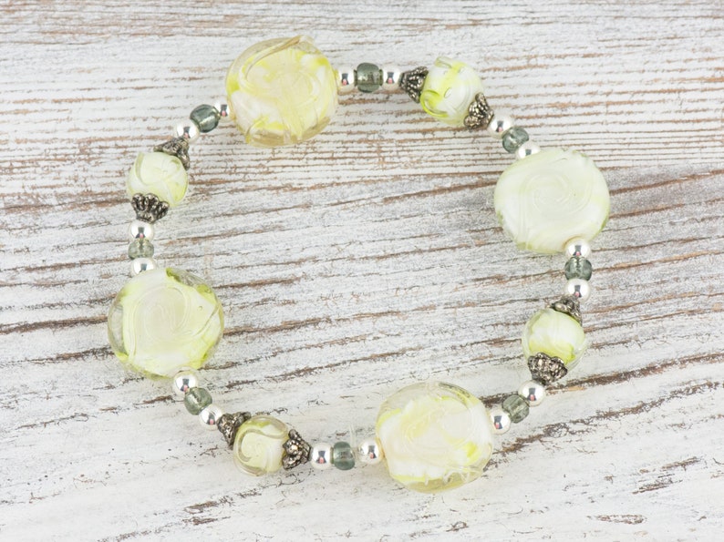 Peut inclure: Un bracelet de perles en verre blanc et vert avec des accents argent&eacute;s. Les perles sont rondes et ont un motif en spirale.