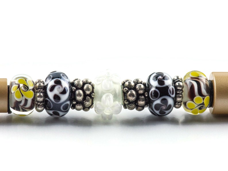 May include: A close-up of a bracelet with a variety of colorful glass beads, including black and white patterned beads, yellow and brown beads, and white beads with a floral design.