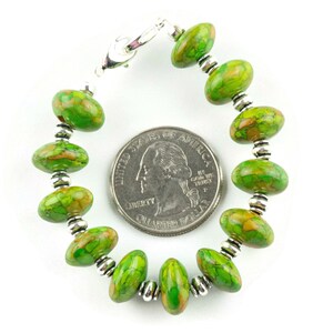 Pode incluir: Pulseira de contas ovais de turquesa verde e laranja com espa&ccedil;adores prateados e fecho prateado. A pulseira est&aacute; ao lado de uma moeda de euro para compara&ccedil;&atilde;o de tamanho.