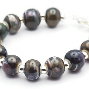 May include: A bracelet made of brown and black ceramic beads with silver accents. The beads have a mottled, marbled effect.