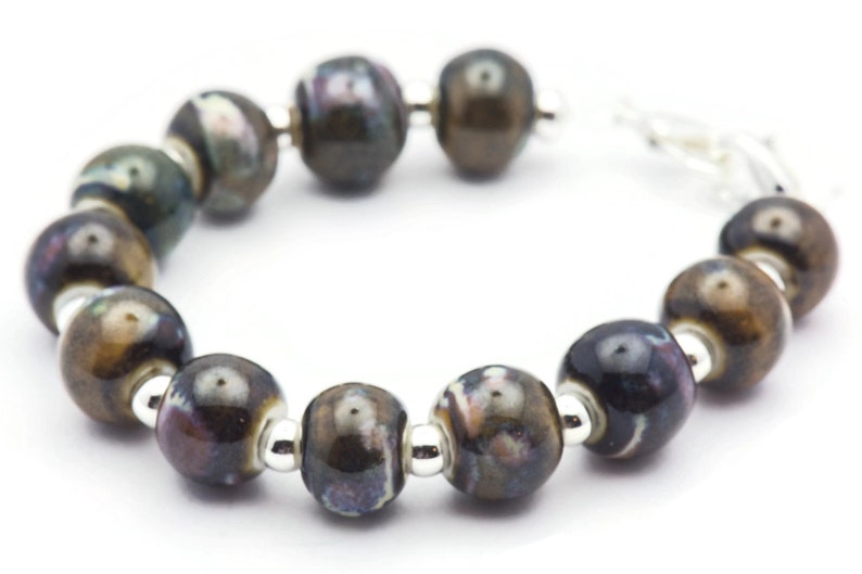 May include: A bracelet made of brown and black ceramic beads with silver accents. The beads have a mottled, marbled effect.
