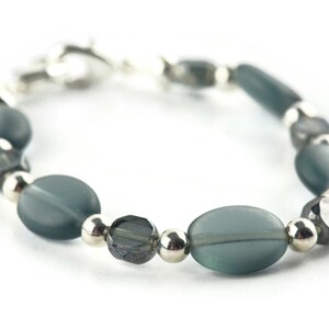 Pu&ograve; includere: Un braccialetto con perline ovali e sfaccettate grigio-verdi, alternate a piccole perline rotonde color argento. Il braccialetto &egrave; assicurato con una chiusura color argento. Le perline hanno un aspetto smerigliato.