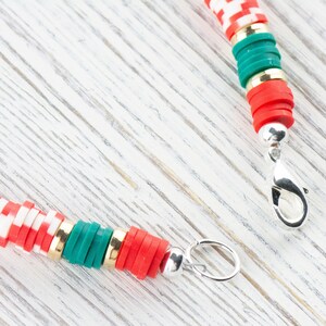 May include: A red, white, and green beaded necklace with a silver clasp. The beads are stacked and have a checkered pattern.