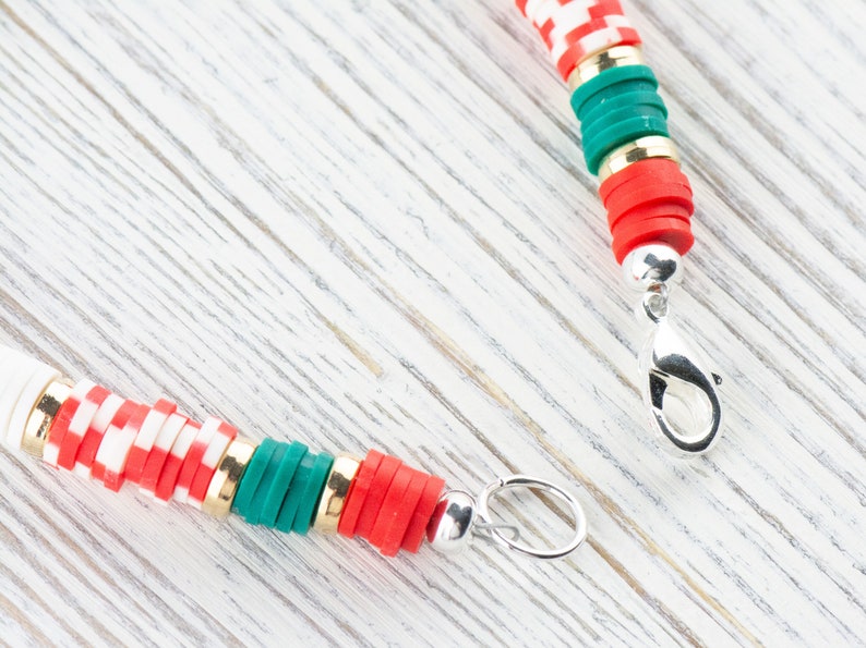 May include: A red, white, and green beaded necklace with a silver clasp. The beads are stacked and have a checkered pattern.