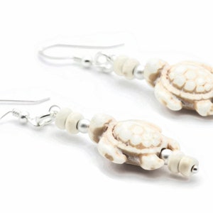 May include: A pair of white turtle earrings with silver hooks and beads. The turtles are detailed with a textured shell and have a white and brown colour scheme.