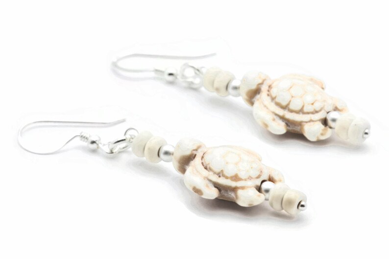 May include: A pair of white turtle earrings with silver hooks and beads. The turtles are detailed with a textured shell and have a white and brown colour scheme.