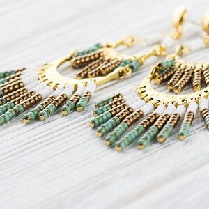 May include: A pair of gold hoop earrings with a fringe of white, brown, and green beads.