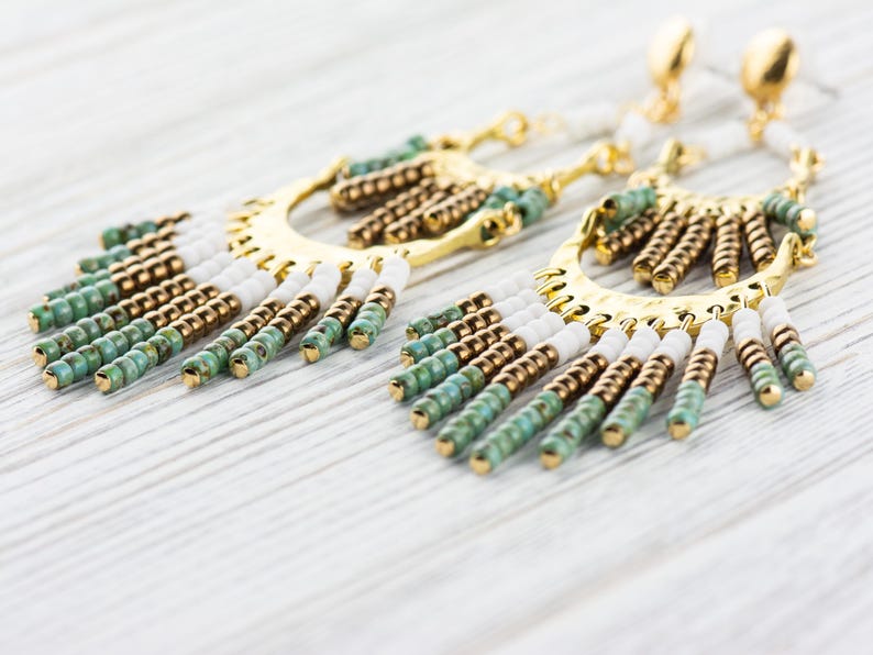 May include: A pair of gold hoop earrings with a fringe of white, brown, and green beads.