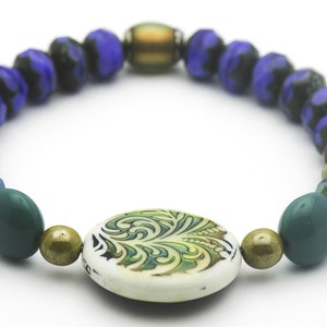 Puede incluir: Un brazalete de cuentas multicolores con un dije de dise&ntilde;o floral verde, blanco y dorado. El brazalete presenta cuentas azules, verdes, marrones y doradas.