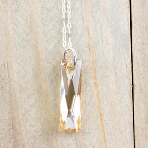 May include: A silver chain necklace with a long, rectangular, light amber crystal pendant.