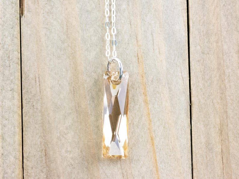 May include: A silver chain necklace with a long, rectangular, light amber crystal pendant.