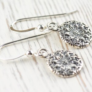 May include: A pair of silver dangle earrings with a delicate floral design. The earrings have a simple hook closure.