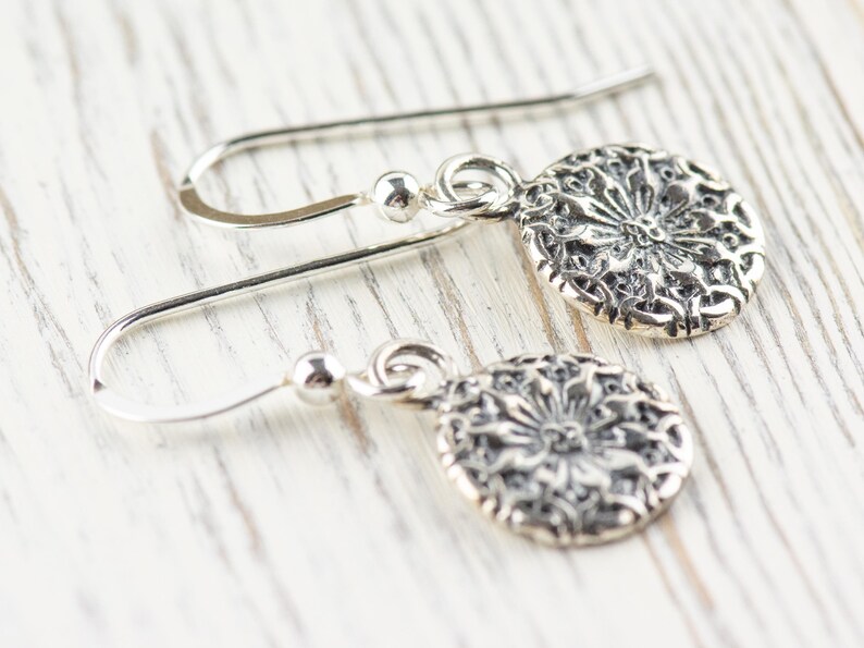 May include: A pair of silver dangle earrings with a delicate floral design. The earrings have a simple hook closure.