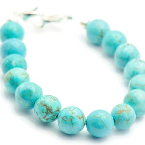 May include: A turquoise beaded bracelet with a silver clasp. The beads are round and have a marbled pattern.