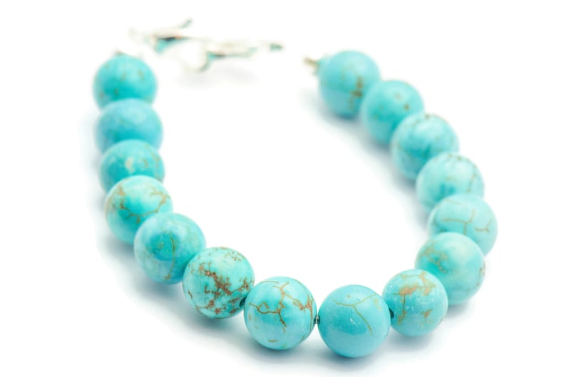 May include: A turquoise beaded bracelet with a silver clasp. The beads are round and have a marbled pattern.