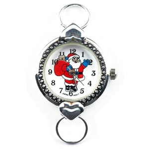 Peut inclure: Une montre argent&eacute;e avec un cadran blanc repr&eacute;sentant un P&egrave;re No&euml;l en dessin anim&eacute; tenant un sac de cadeaux. La montre a un fermoir en forme de c&oelig;ur et une cha&icirc;ne argent&eacute;e.