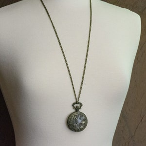 Pu&ograve; includere: Una collana a catena di bronzo con un ciondolo a forma di orologio da tasca rotondo in stile antico. Il quadrante dell'orologio ha un design decorativo.