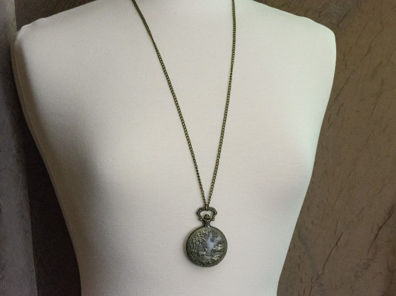 Pu&ograve; includere: Una collana a catena di bronzo con un ciondolo a forma di orologio da tasca rotondo in stile antico. Il quadrante dell'orologio ha un design decorativo.