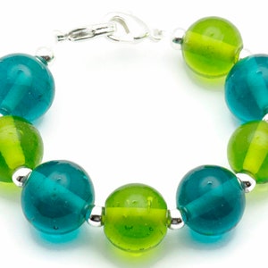 Puede incluir: Un brazalete hecho de cuentas de vidrio alternas de color verde azulado y verde con separadores plateados y un cierre plateado.