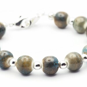 Pode incluir: Um bracelete de prata com contas de cer&acirc;mica azul e marrom. As contas t&ecirc;m um efeito manchado, marmorizado.