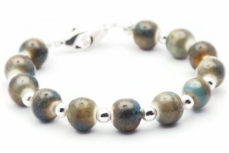 Pode incluir: Um bracelete de prata com contas de cer&acirc;mica azul e marrom. As contas t&ecirc;m um efeito manchado, marmorizado.