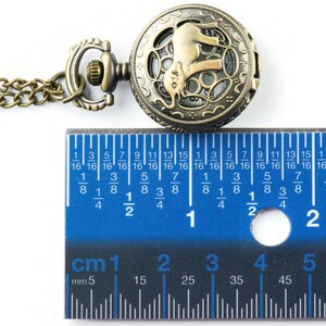 May include: A bronze pocket watch with an elephant design on the face. The watch is 2.5 cm in diameter and has a chain attached.