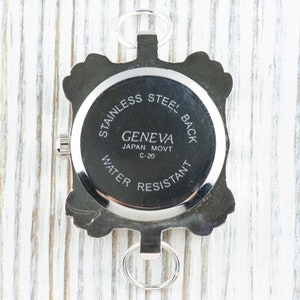 May include: The back of a silver watch with a round face and a silver band. The watch face has the text "STAINLESS STEEL BACK GENEVA JAPAN MOVT C-20 WATER RESISTANT" printed on it.