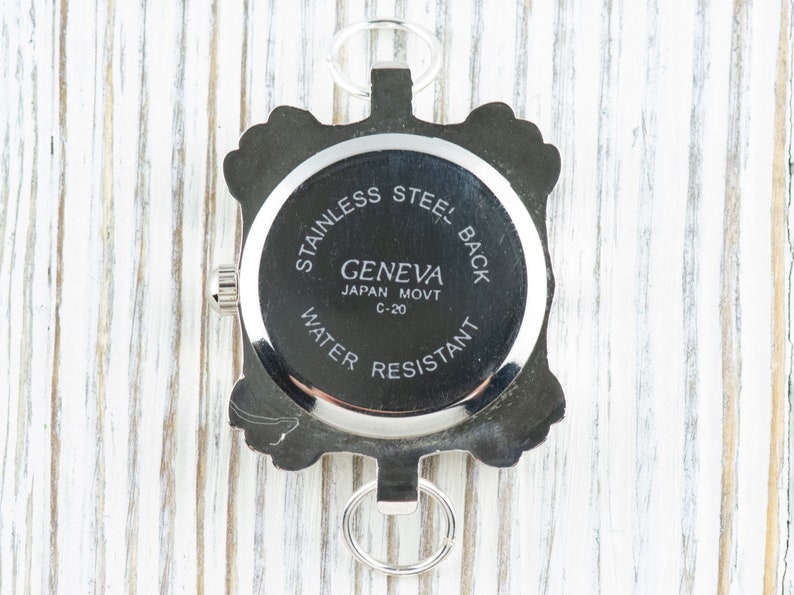 May include: The back of a silver watch with a round face and a silver band. The watch face has the text "STAINLESS STEEL BACK GENEVA JAPAN MOVT C-20 WATER RESISTANT" printed on it.
