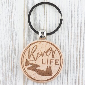 May include: A wooden keyring with a silver key ring. The keyring is round and has a river and trees engraved on it. The text "River Life" is also engraved on the keyring.
