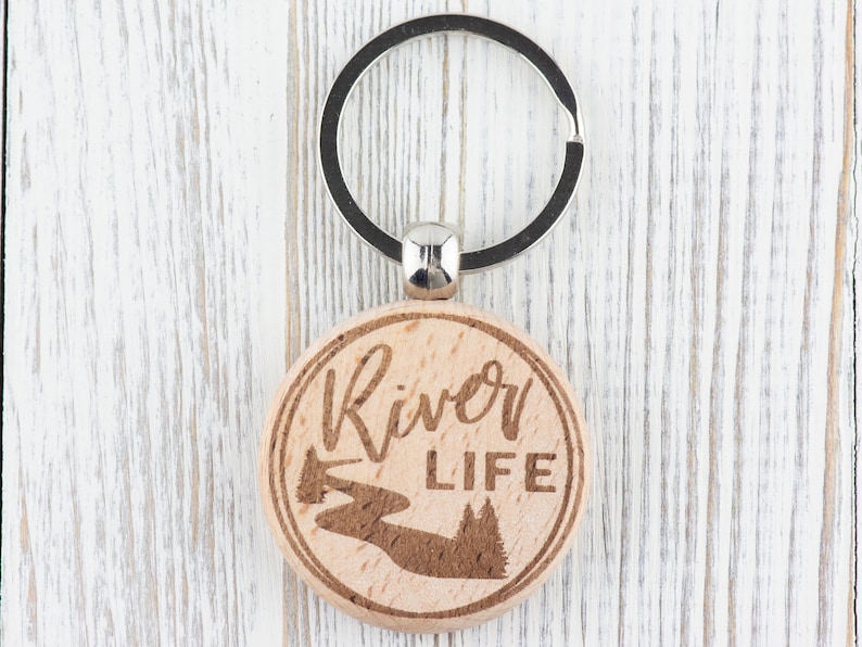 May include: A wooden keyring with a silver key ring. The keyring is round and has a river and trees engraved on it. The text "River Life" is also engraved on the keyring.