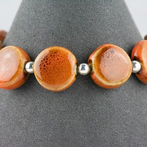 May include: A bracelet made of orange ceramic beads with silver spacers. The beads have a speckled texture.