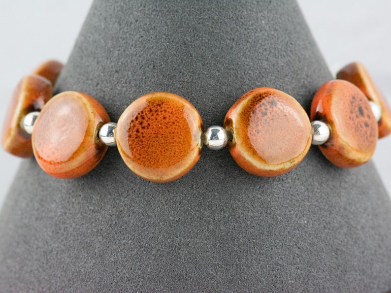May include: A bracelet made of orange ceramic beads with silver spacers. The beads have a speckled texture.