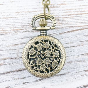 K&ouml;nnte beinhalten: Antiker bronzefarbener Taschenuhr-Anh&auml;nger mit aufwendigem floralem Filigran-Design. Die Uhr verf&uuml;gt &uuml;ber eine detaillierte durchbrochene Abdeckung und eine dekorative obere Schlaufe zum Aufh&auml;ngen. Die Uhr h&auml;ngt an einer passenden Kette.