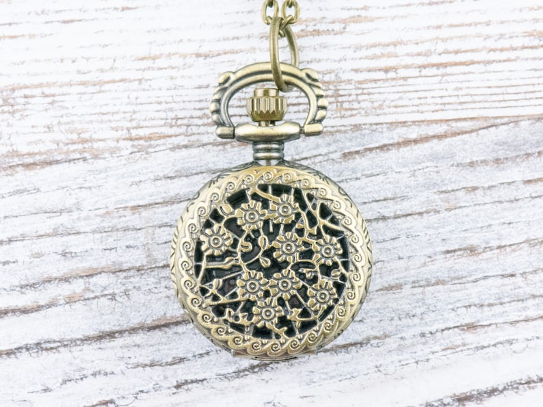 K&ouml;nnte beinhalten: Antiker bronzefarbener Taschenuhr-Anh&auml;nger mit aufwendigem floralem Filigran-Design. Die Uhr verf&uuml;gt &uuml;ber eine detaillierte durchbrochene Abdeckung und eine dekorative obere Schlaufe zum Aufh&auml;ngen. Die Uhr h&auml;ngt an einer passenden Kette.