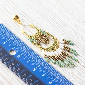 May include: Gold and turquoise beaded dangle earrings with a hammered metal hoop. The earrings are approximately 3 inches long.