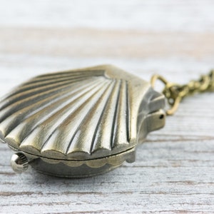 May include: A silver-toned seashell pendant necklace with a chain. The pendant is shaped like a seashell with a detailed design.