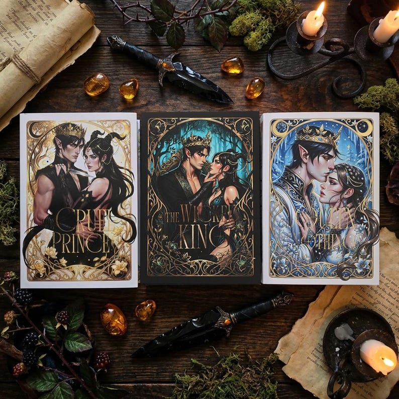 Puede incluir: Tres portadas de libros de fantas&iacute;a con ilustraciones de un hombre y una mujer, con los t&iacute;tulos "The Cruel Prince", "The Wicked King" y "The Queen of Nothing". Una daga negra y piedras de color &aacute;mbar est&aacute;n dispuestas alrededor de los libros sobre una superficie de madera.