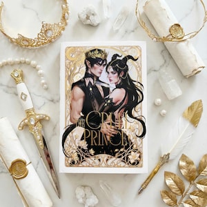 Puede incluir: Un libro titulado "The Cruel Prince" con una ilustraci&oacute;n de fantas&iacute;a de un hombre y una mujer. La imagen incluye una daga decorativa, coronas, una pluma y pergaminos, todos con detalles dorados. Tambi&eacute;n hay cristales y perlas.