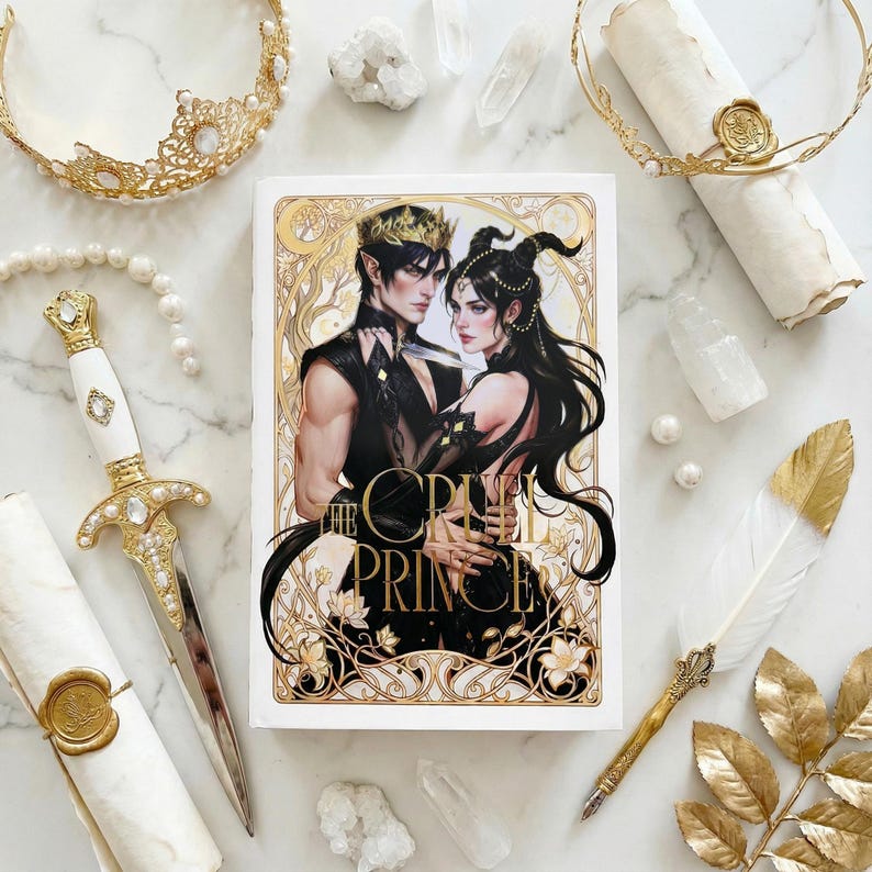 Puede incluir: Un libro titulado "The Cruel Prince" con una ilustraci&oacute;n de fantas&iacute;a de un hombre y una mujer. La imagen incluye una daga decorativa, coronas, una pluma y pergaminos, todos con detalles dorados. Tambi&eacute;n hay cristales y perlas.