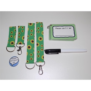 May include: A selection of accessories featuring green sunflower-patterned lanyards, a button with the text "Please don't touch me", a small notepad with the text "Please can I / we", and a black and white marker.