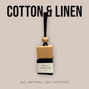 Könnte beinhalten: Ein Auto-Lufterfrischer mit schwarzem Kordel und Holzakzenten. Das Produkt hat einen Holzquader und einen kleinen schwarzen Behälter mit dem Aufdruck "COTTON & LINEN". Der Text "ALL-NATURAL CAR DIFFUSER" steht unten.