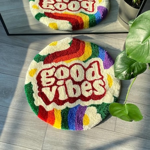 May include: Two round, colorful, fluffy rugs with the words "Good Vibes" and "Good Vibes" in red and white. The rugs have a rainbow border and white daisy-like shapes.