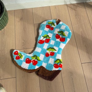 May include: A blue and white checkered rug shaped like a cowboy boot with red cherries embroidered on it.