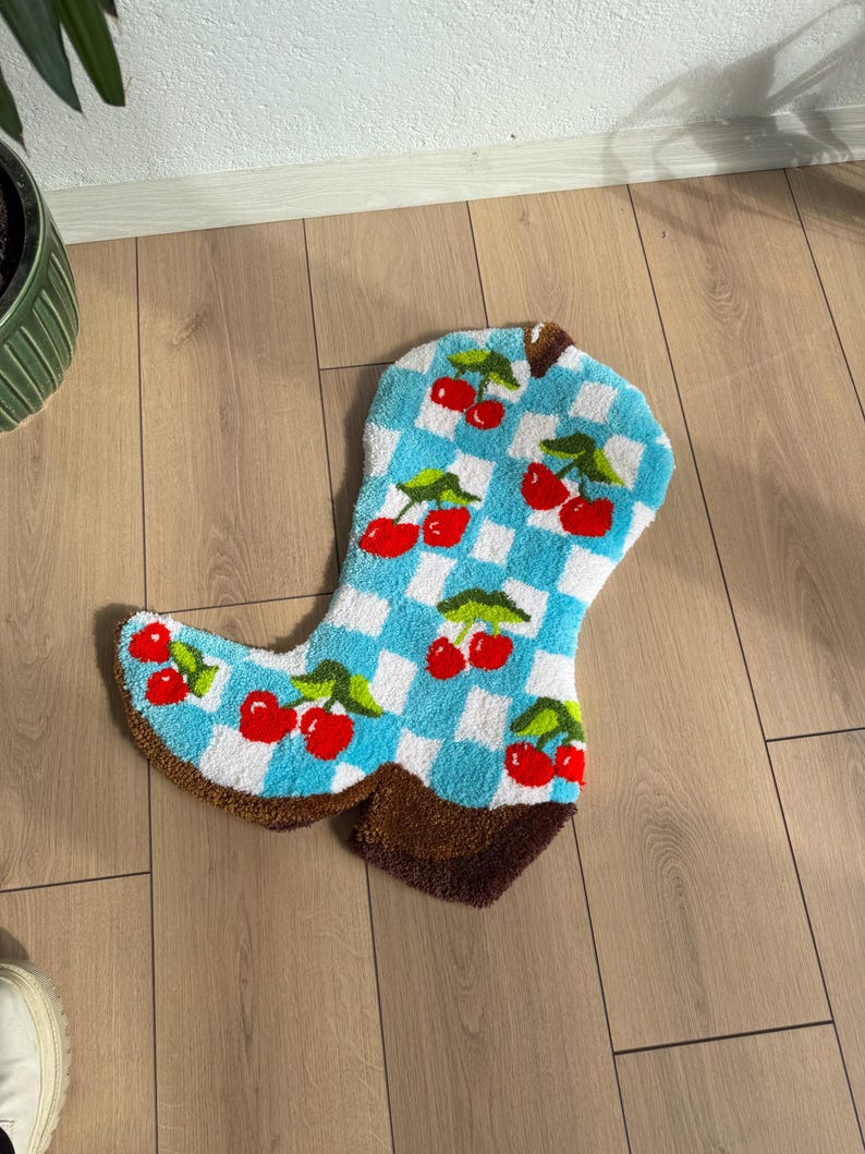 May include: A blue and white checkered rug shaped like a cowboy boot with red cherries embroidered on it.