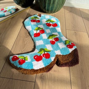 May include: A blue and white checkered boot rug with red cherries. The rug is made of a soft, plush material and is perfect for adding a touch of whimsy to any room.