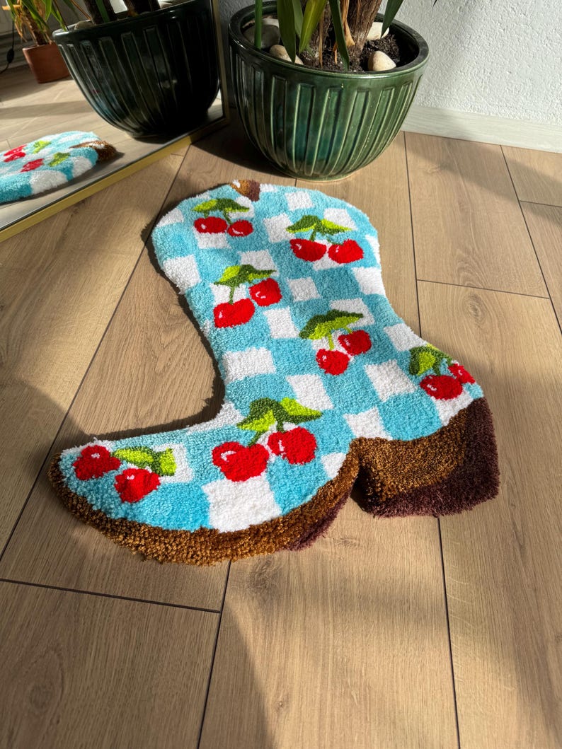 May include: A blue and white checkered boot rug with red cherries. The rug is made of a soft, plush material and is perfect for adding a touch of whimsy to any room.