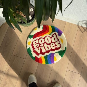 May include: A round, fluffy rug with a rainbow border and the words "good vibes" in red letters on a white background.