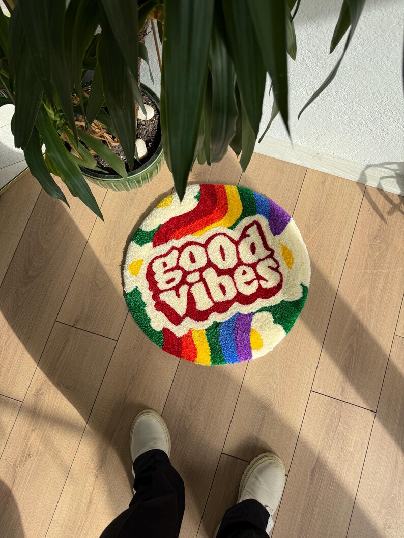 May include: A round, fluffy rug with a rainbow border and the words "good vibes" in red letters on a white background.