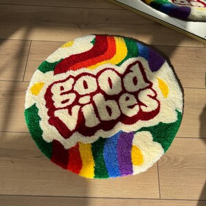 May include: A round, white, fluffy rug with a rainbow design and the words "good vibes" in red lettering.