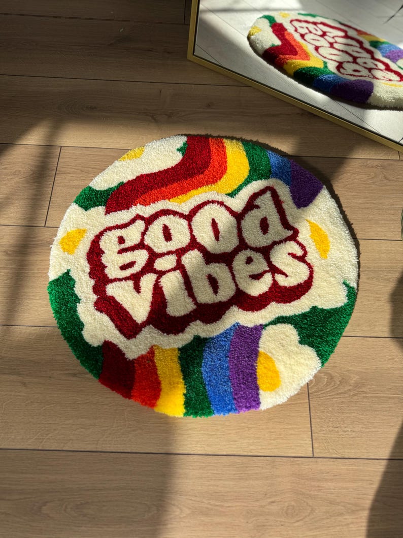 May include: A round, white, fluffy rug with a rainbow design and the words "good vibes" in red lettering.